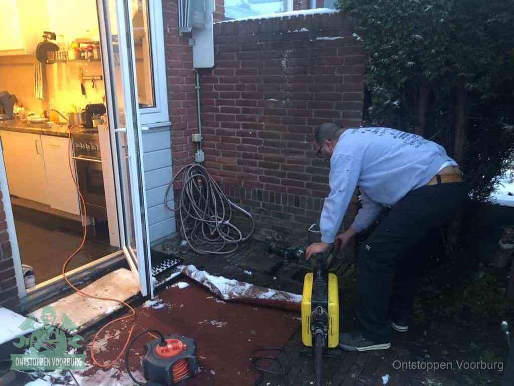 Een monteur werkt buiten bij een open riool-/grondput met een elektrische ontstoppingsmachine om een verborgen afvoerprobleem op te sporen in Voorburg
