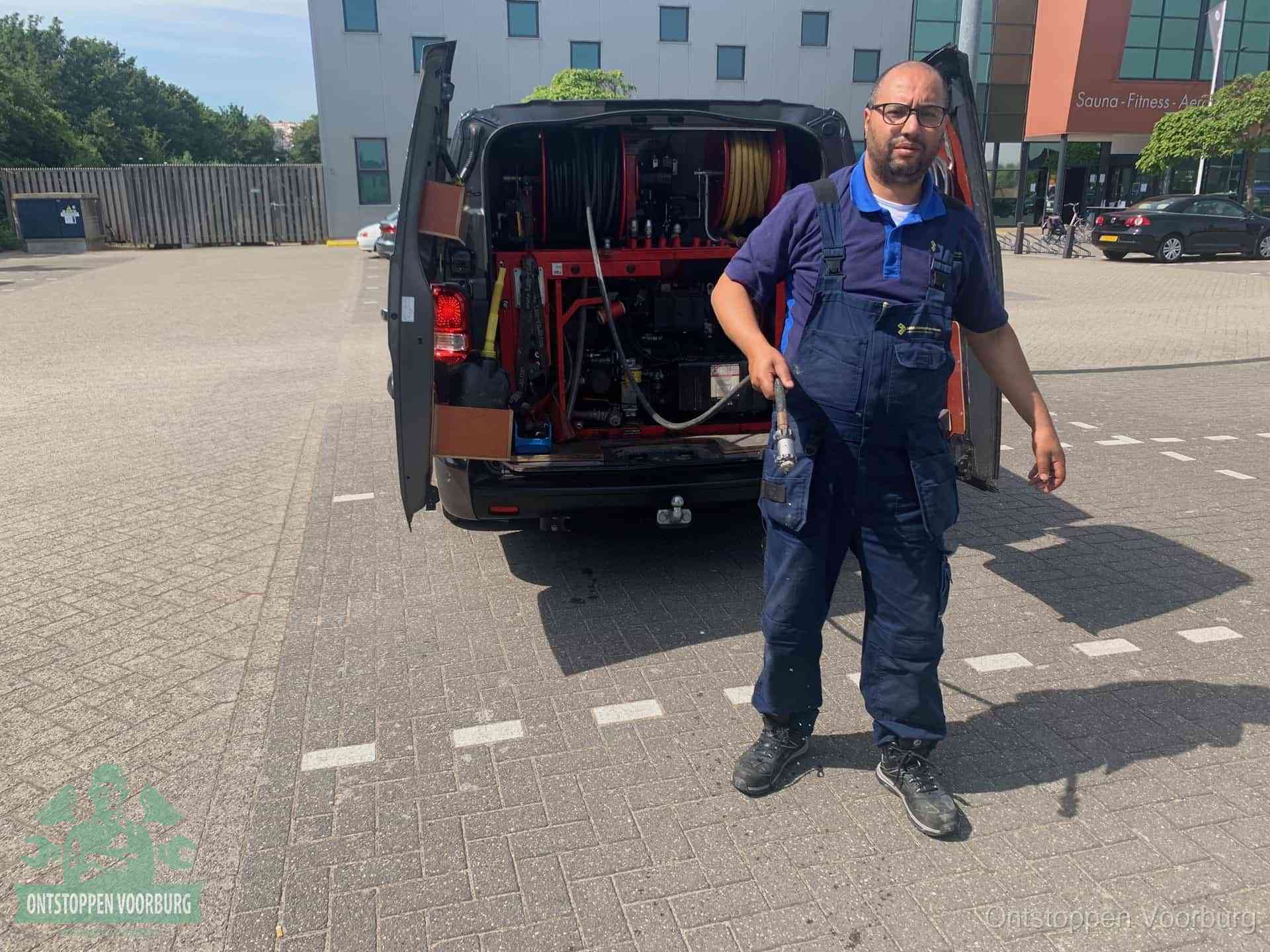 Een monteur bij zijn bestelbus met een hogedruk- en rioolreinigingsunit, klaar om de oorzaak van terugkerende wc-verstoppingen aan te pakken in Voorburg