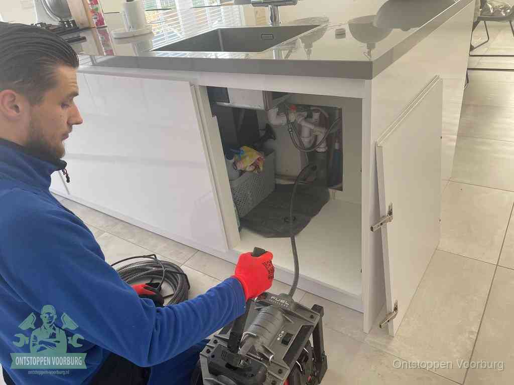 Monteur ontstopt met een veermachine een verstopte afvoer onder de gootsteen in Voorburg