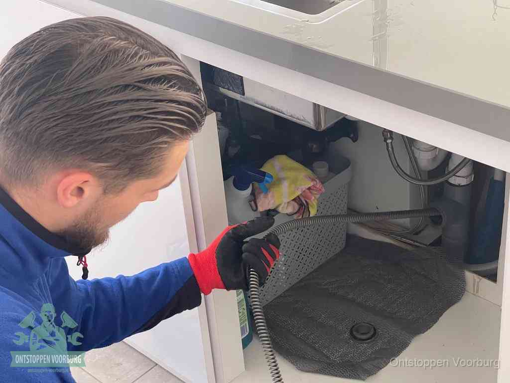 Een monteur voert een flexibele ontstoppingsveer in de afvoer om een verstopping voorbij de bocht van het toilet te bereiken in Voorburg