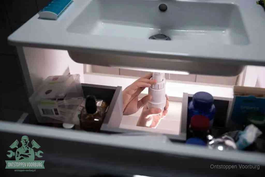 Een pompfles met zeep boven een wastafel in de toiletruimte, de warm water en afwasmiddel-methode om de wc te ontstoppen in Voorburg