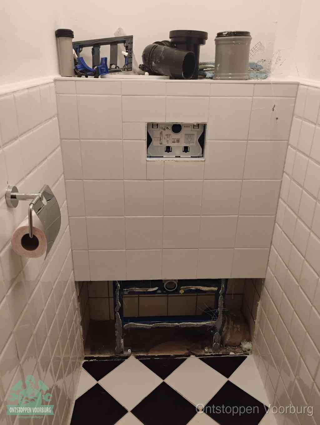 Een toiletruimte waar het hangtoilet en de inbouwreservoir-onderdelen zijn vrijgelegd voor onderhoud, periodiek nazicht voorkomt een wc-verstopping in Voorburg